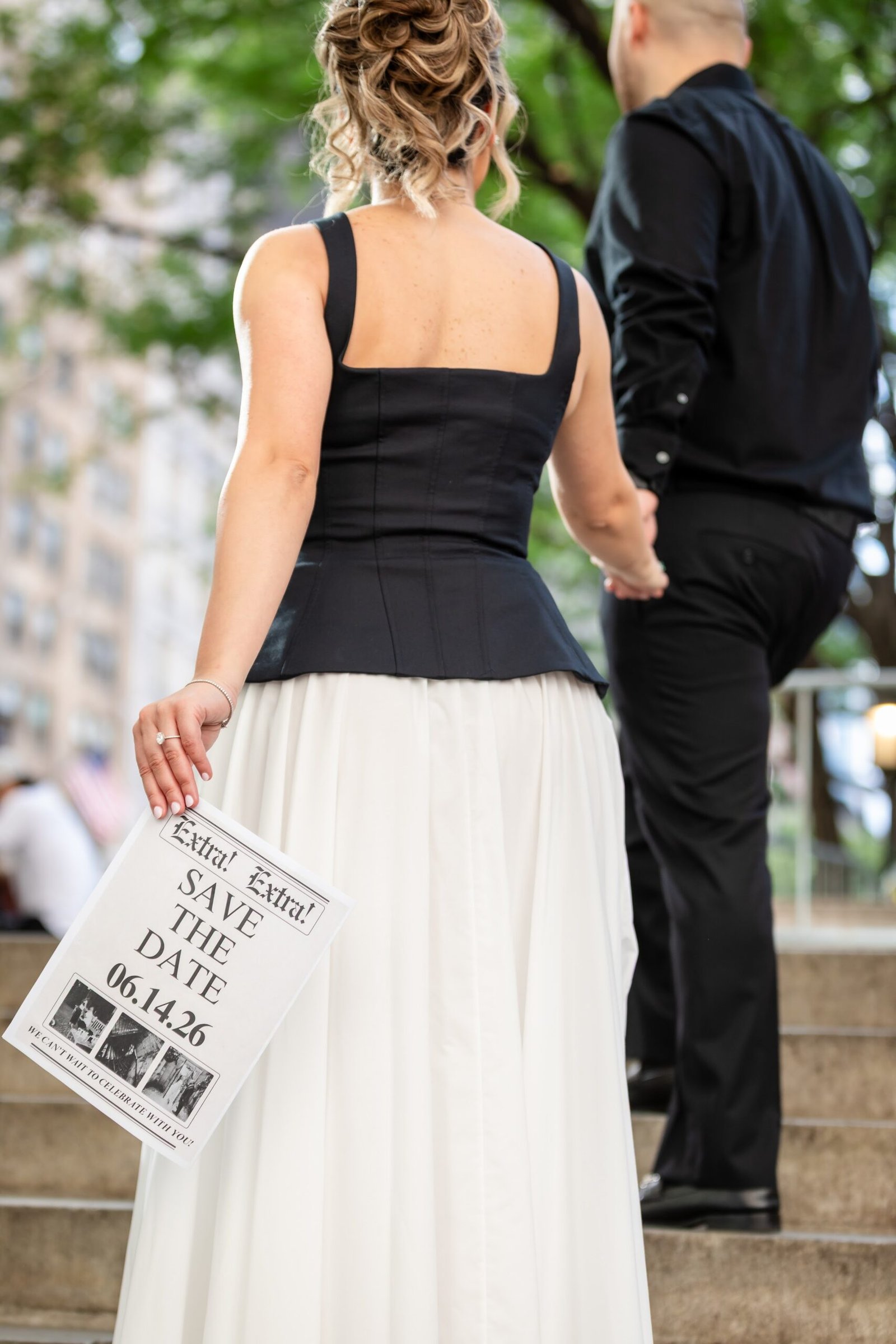 Detail of the save the date card held behind the bride to be
