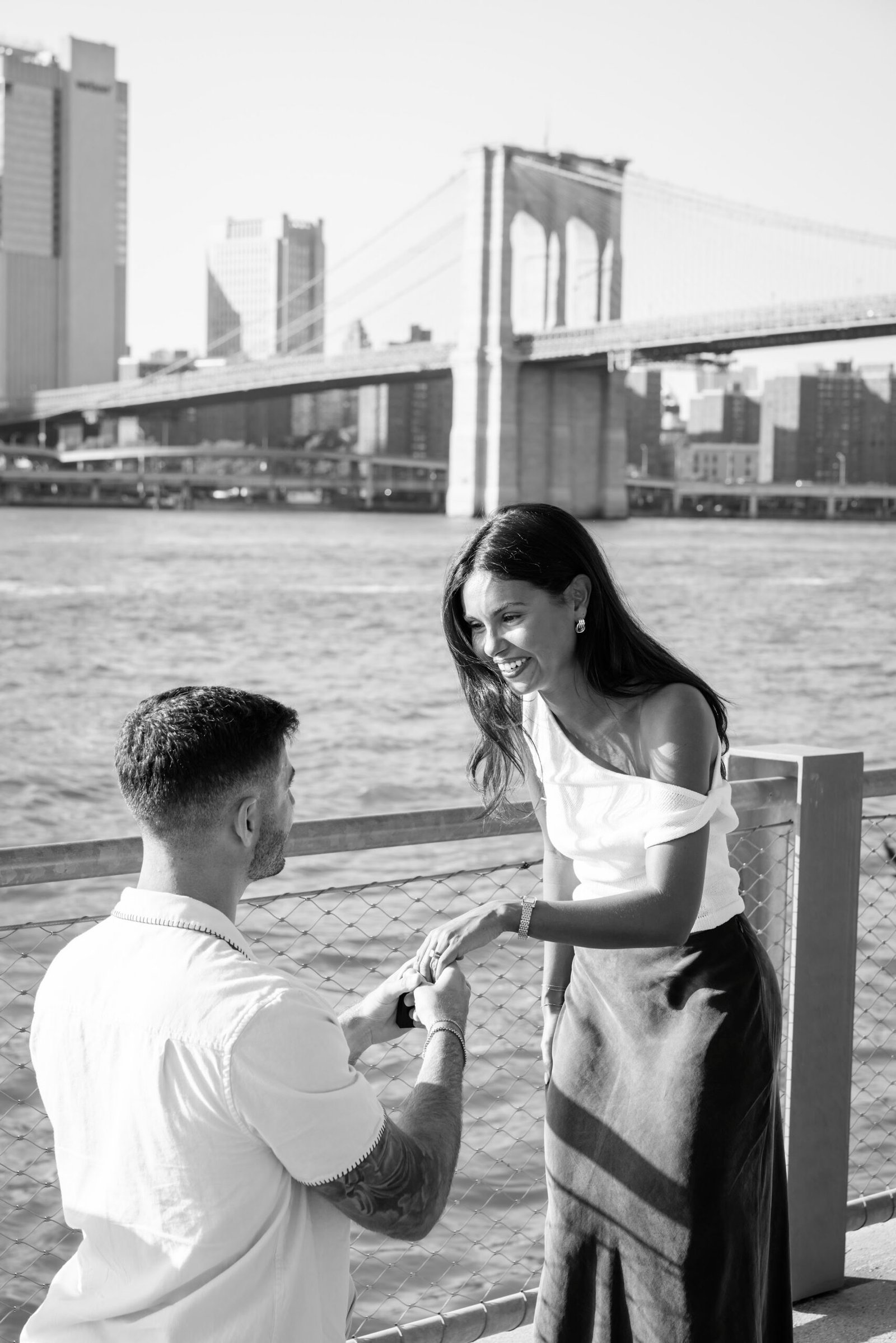 Black and white photograph of a marriage proposal by the Brooklyn Bridge