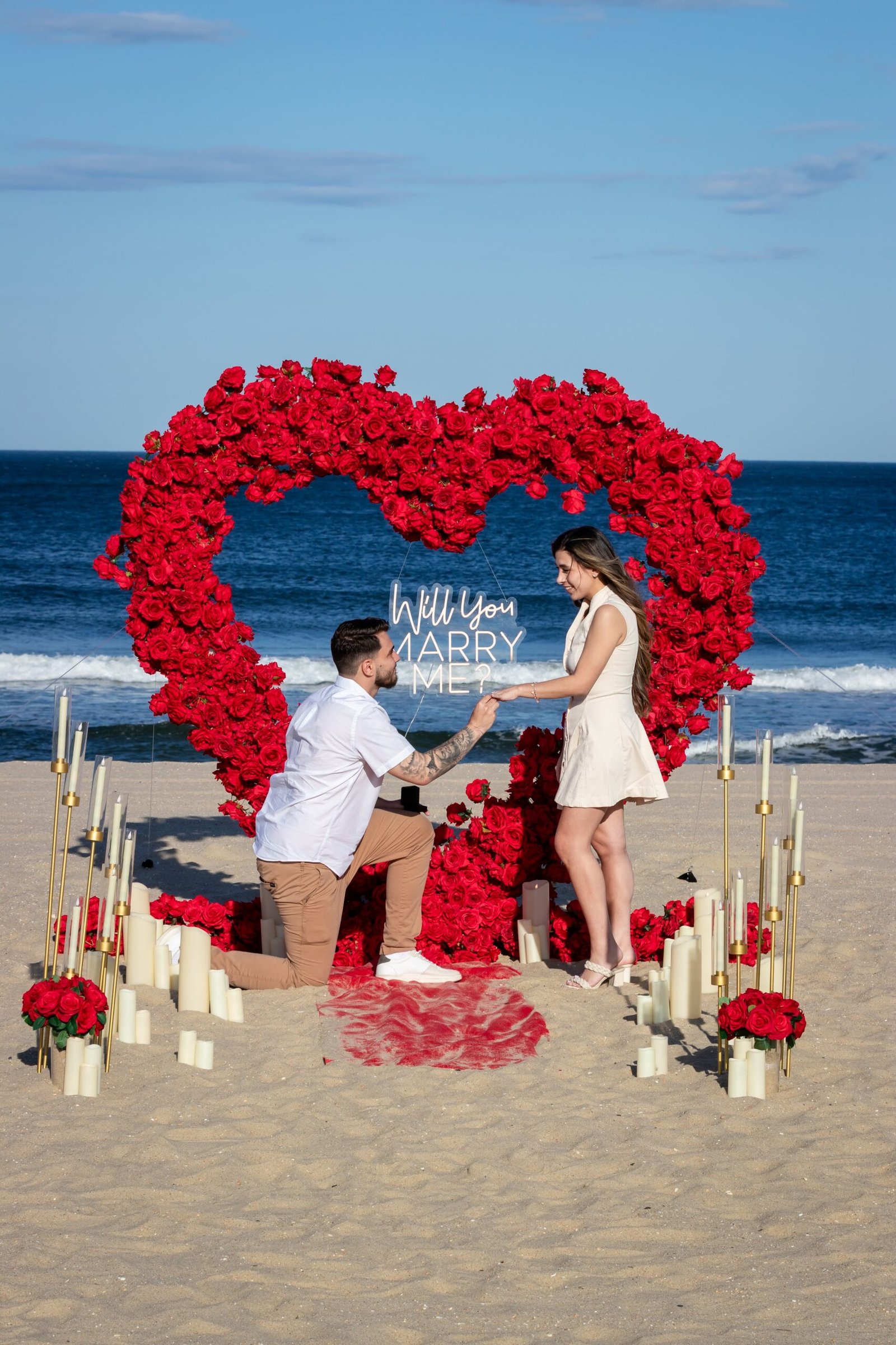 Beachside proposal beneath a heart shaped red rose arch