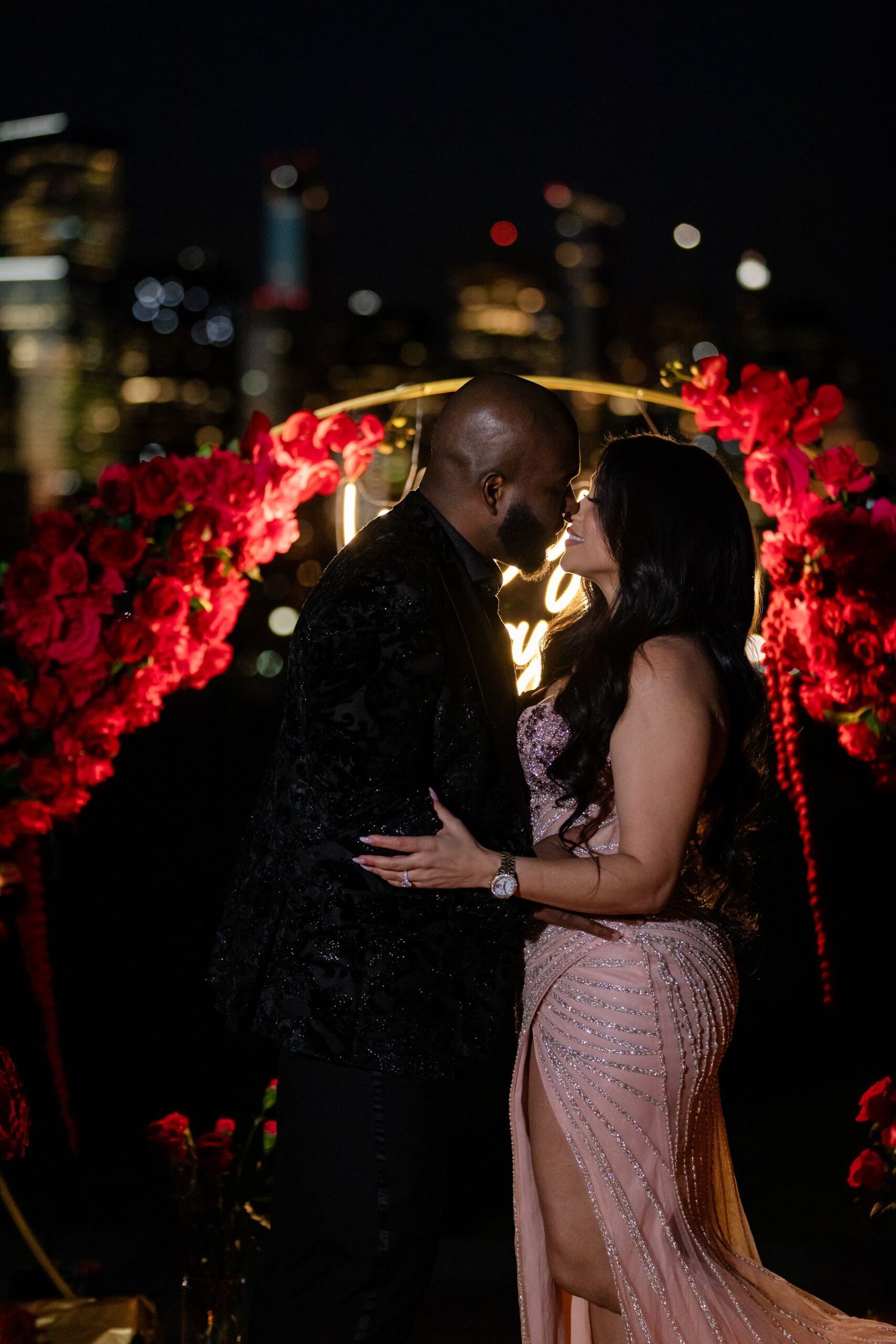 Couple sharing a kiss beneath the red rose arch